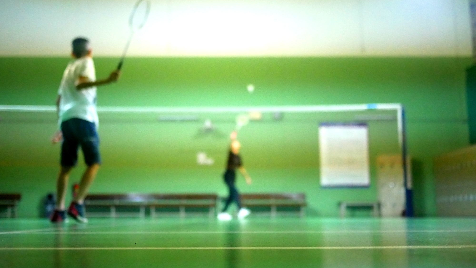 Blurred kid playing badminton in court with friend.